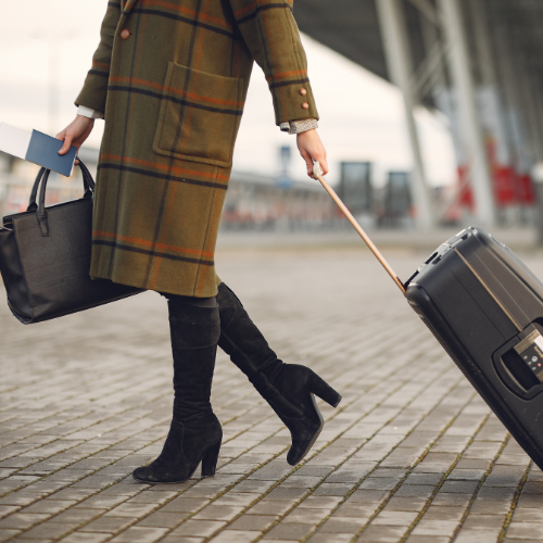 Woman in coat pulling luggage on sidewalk.